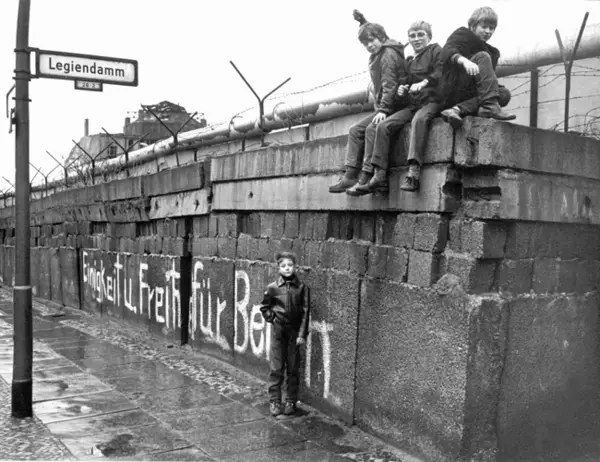 A group of children sits on the Berlin Wall at the 'Legiendamm' in the West Berlin borough Kreuzberg, March 1972. A white graffiti translates 'Unity and Freedom for Berlin'.